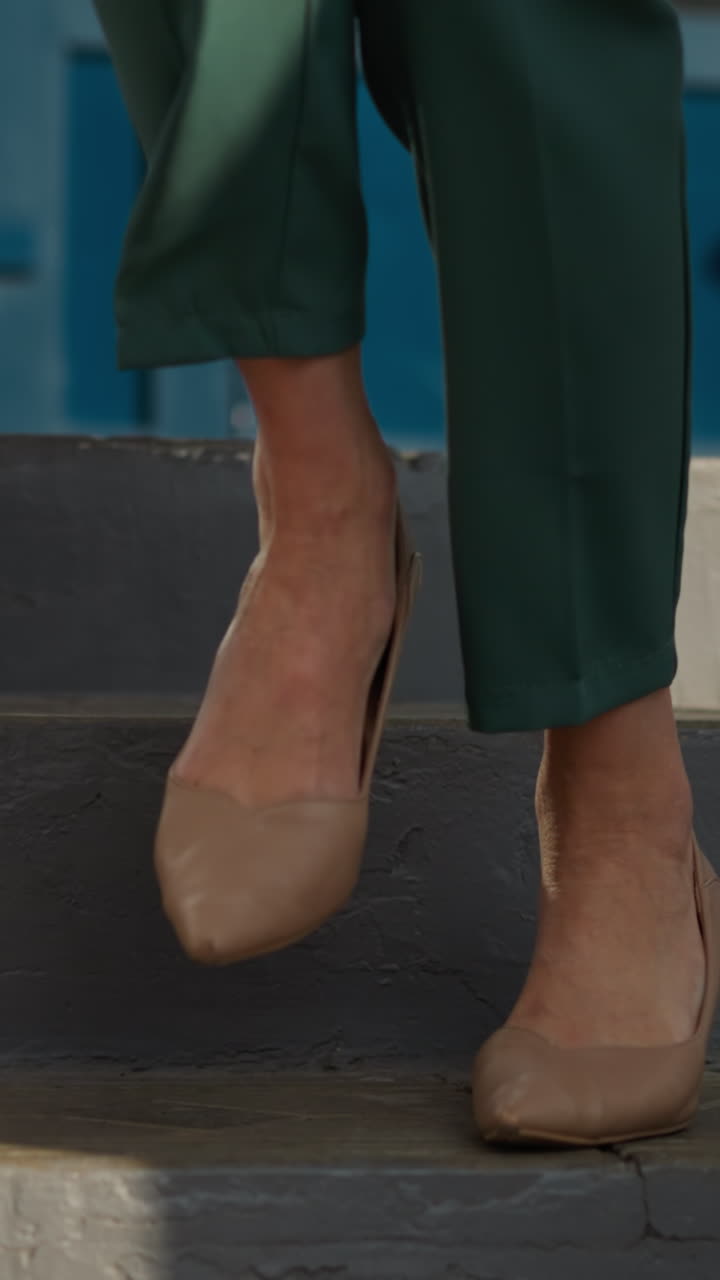 las piernas femeninas en zapatos de tacón alto beige bajan las escaleras. mujer joven en traje de negocios verde deja el edificio moviéndose con confianza en un día soleado de primer plano