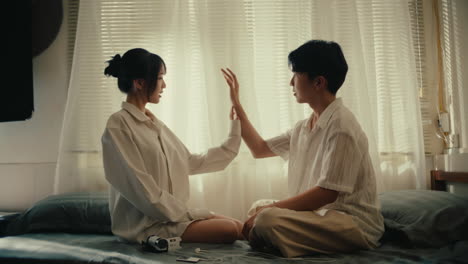 couple of young lovers sitting cross leg in front of each other playing together touching the hands in the living room couch