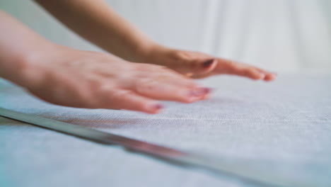 person-adjusts-white-fabric-on-table-with-chalk-and-ruler