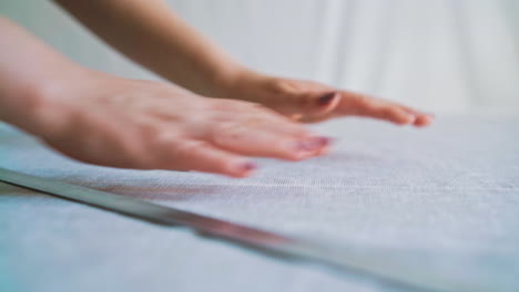 person adjusts white fabric on table with chalk and ruler