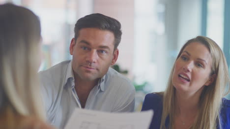 Close-Up-Of-Business-Team-Having-Meeting-Sitting-Around-Table-In-Modern-Open-Plan-Office