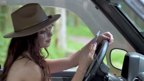 Una-Mujer-Hermosa-Con-Sombrero-Está-Sentada-En-Un-Auto-Y-Enviando-Mensajes-De-Texto-Por-Teléfono