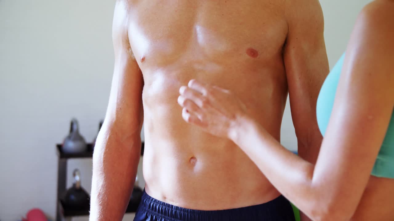 mujer tocando a un hombre musculoso en el gimnasio 4k