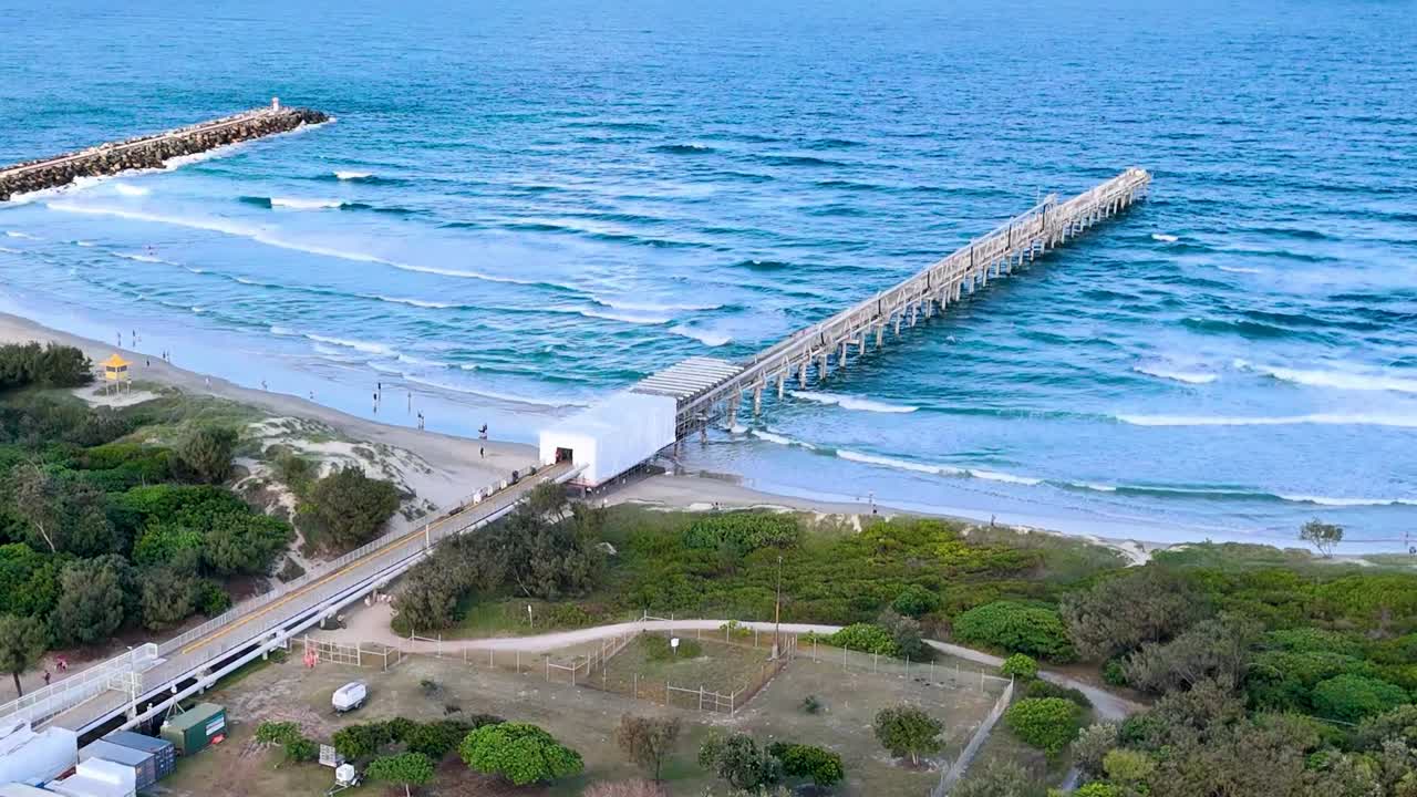 Drone footage showcasing a pier extending into the ocean with adjacent parkland and greenery.