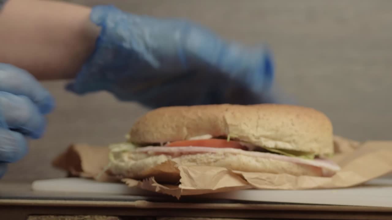 Mani che mettono un tramezzino con insalata in un sacchetto di carta con guanti igienici