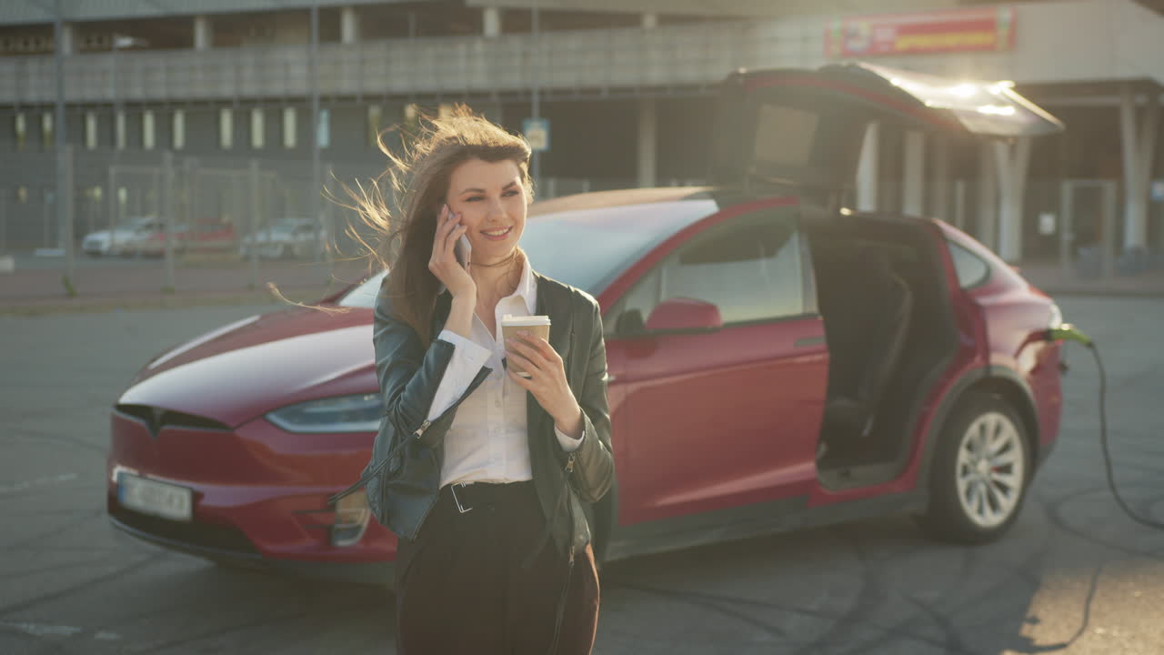 mujer cargando un coche eléctrico y hablando por teléfono