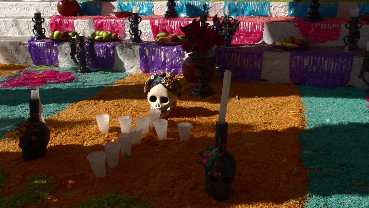 Altare colorato del Día de Muertos con decorazioni a teschio, candele, offerte, frutta e luminosi motivi di segatura in una tradizionale esposizione commemorativa messicana.