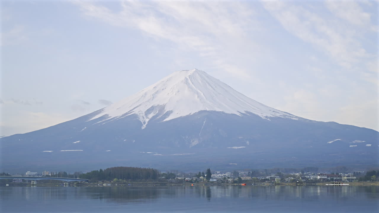 Timelapse of morning over Mount Fuji, illuminating the snow-capped peak and surrounding landscape. Kawaguchiko Lake, Japan
