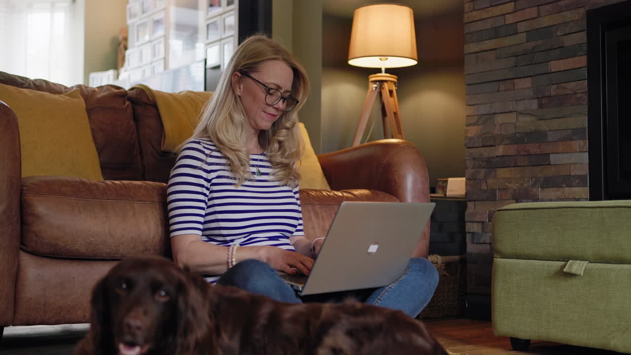 A woman using a laptop in a living room with a dog