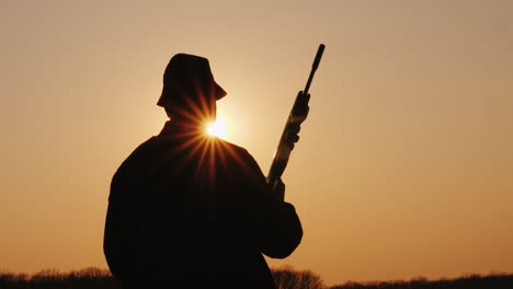 Silhouette-Of-A-Hunter-With-A-Gun-The-Sun's-Rays-Shine-In-His-Face