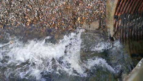 Water-cascading-from-a-drain-in-a-stone-wall-across-a-stony-beach-in-Broad-Haven,-West-Wales