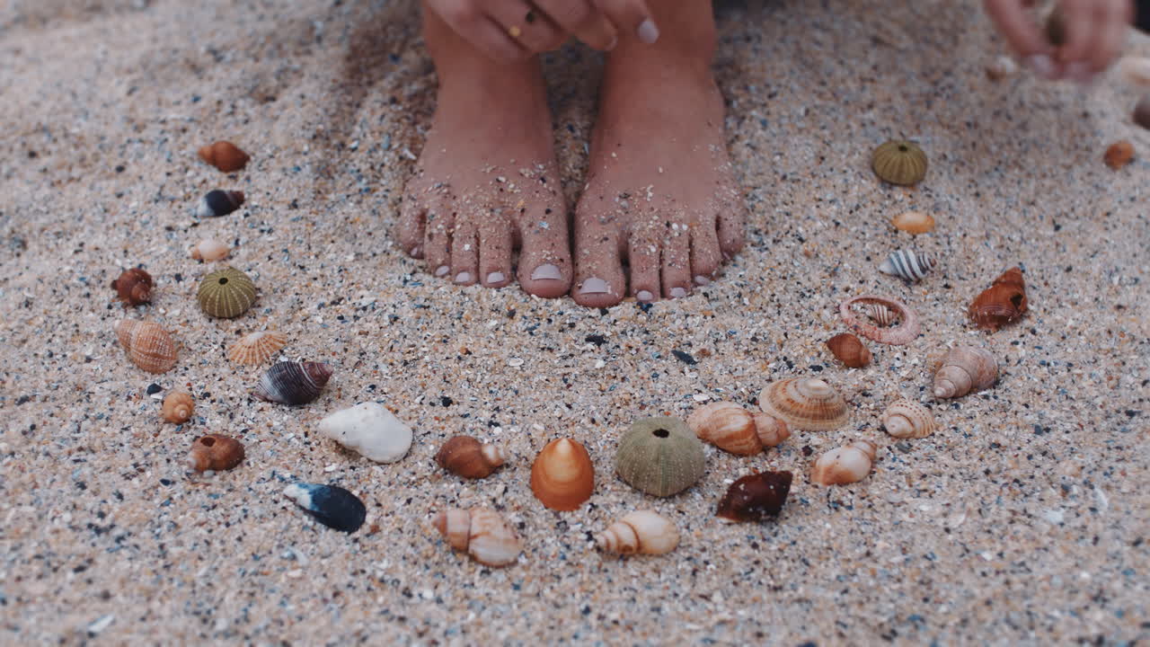 piedi ravvicinati donna che raccoglie conchiglie sulla spiaggia godendo di una bella varietà naturale facendo forma a modello sulla sabbia