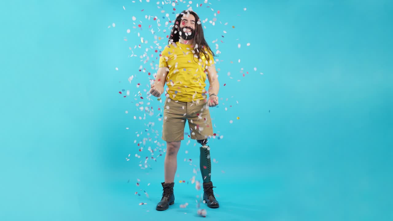 Joyful man with prosthetic leg celebrating with confetti on blue background