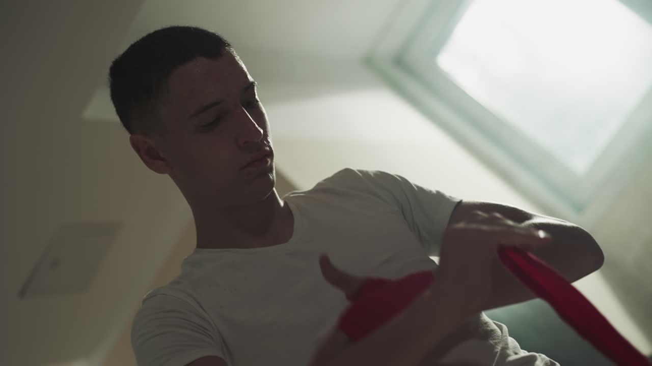 Athlete protects hand with wrap for boxing in combat gym. Thoughtful boxer applies fabric strip for palm and wrist in martial arts club slow motion