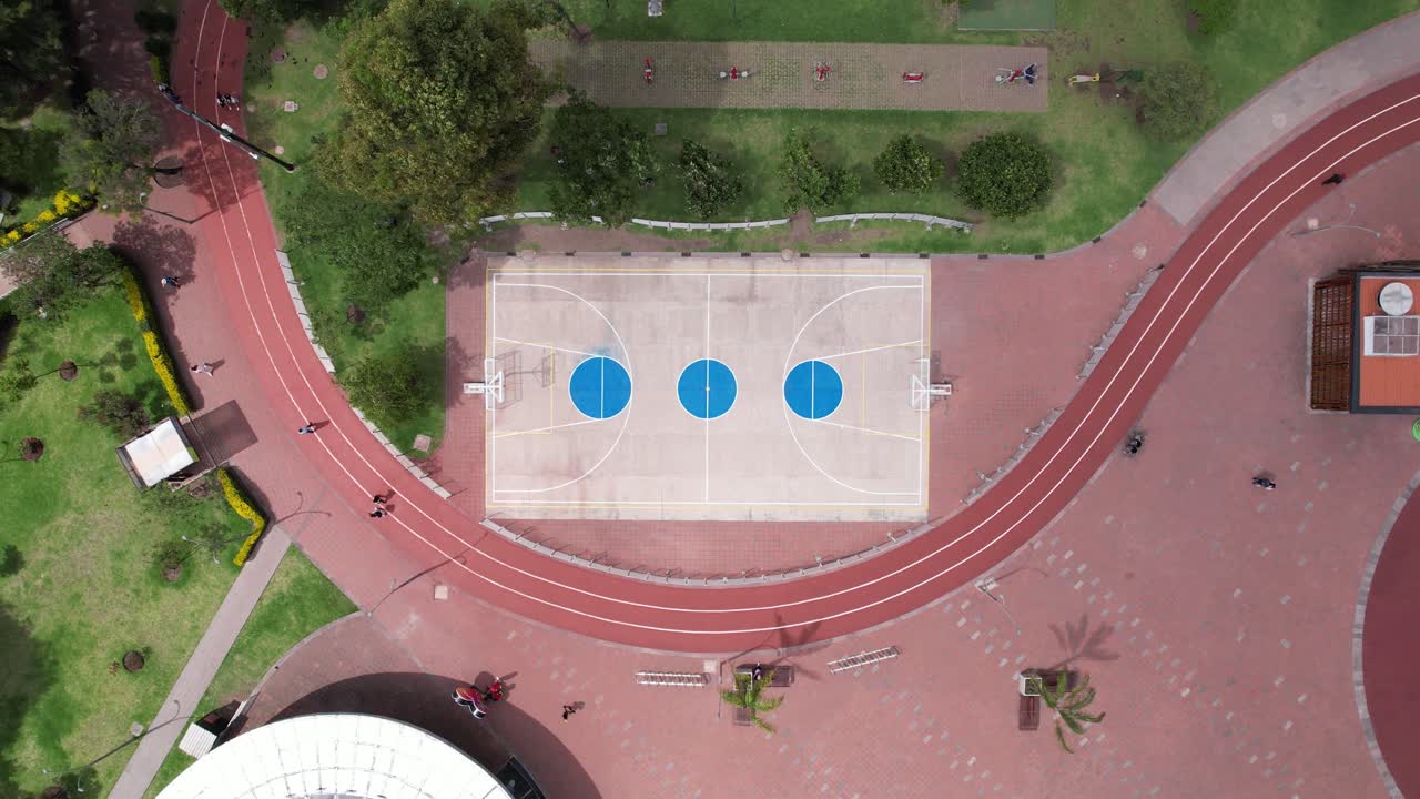 4K drone rising shot of a basketball court in a public park, revealing the surrounding green areas and urban space in a peaceful and active community setting.