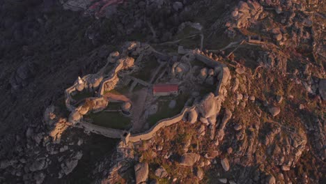Top-down-shot-of-medieval-Castelo-de-Monsanto-on-hill-top-during-sunrise,-aerial