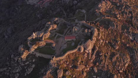 Toma-De-Arriba-Hacia-Abajo-Del-Castelo-Medieval-De-Monsanto-En-La-Cima-De-La-Colina-Durante-El-Amanecer,-Antena