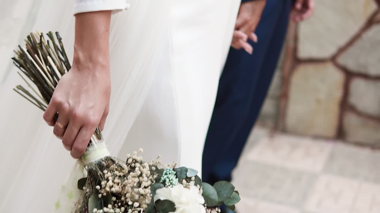 Bride With White Dress Carrying Flowers Bouquet Holding Her Groom's Hand At Wedding Day
