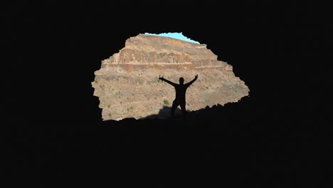 Silhouette of a man with a drone in his hand inside a dark cave and raising his arms