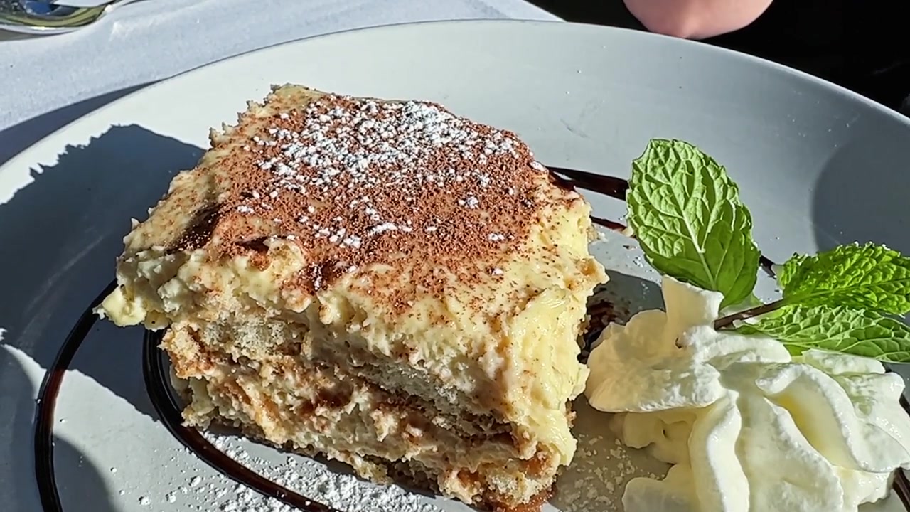 Primo piano di una persona che mangia una deliziosa fetta di tiramisù tradizionale italiano, guarnita con cacao in polvere, menta e panna montata