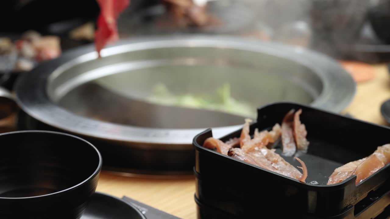 Hand dips sliced beef into steaming hotpot broth, close-up, warm lighting, shallow depth of field