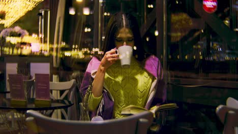 woman reading and drinking coffee in a cozy cafe at night