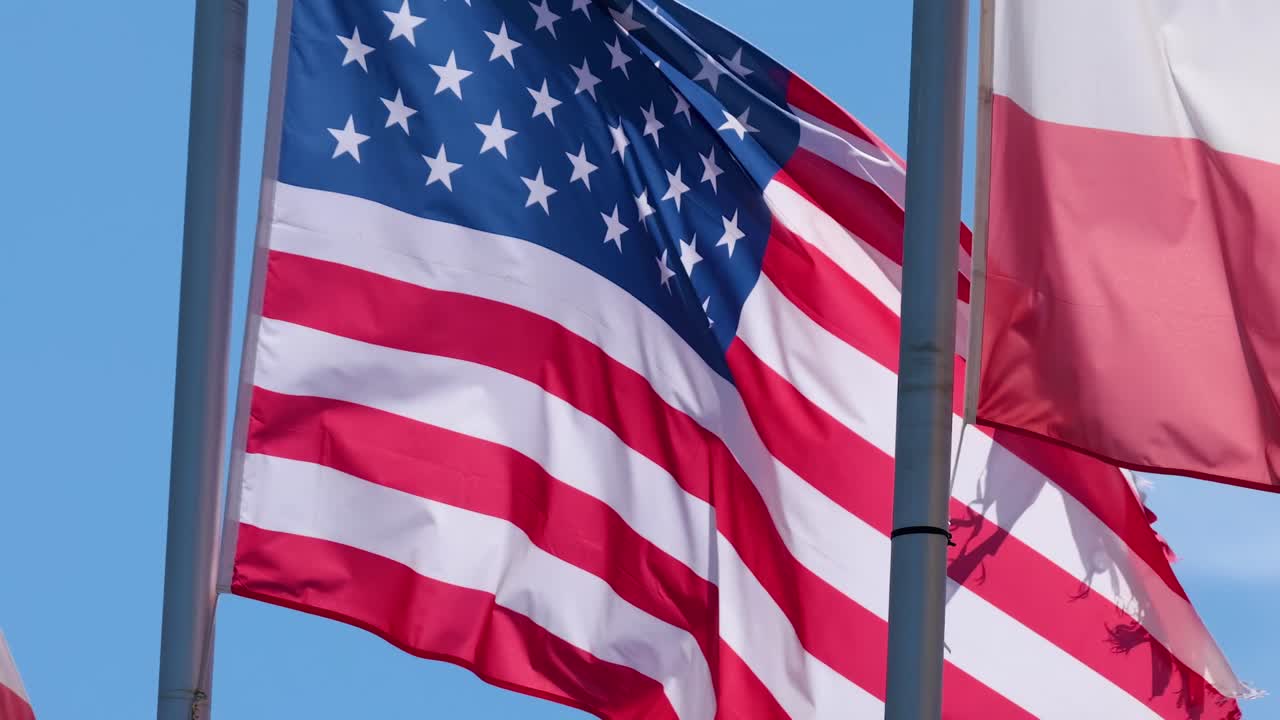 Close-up of American and Polish flags fluttering against a clear blue sky.