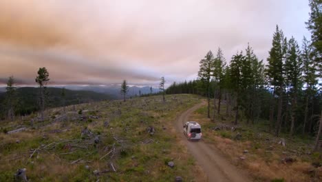 drone follows a camper van down a dirt road in the mountain at sunset during wildfires