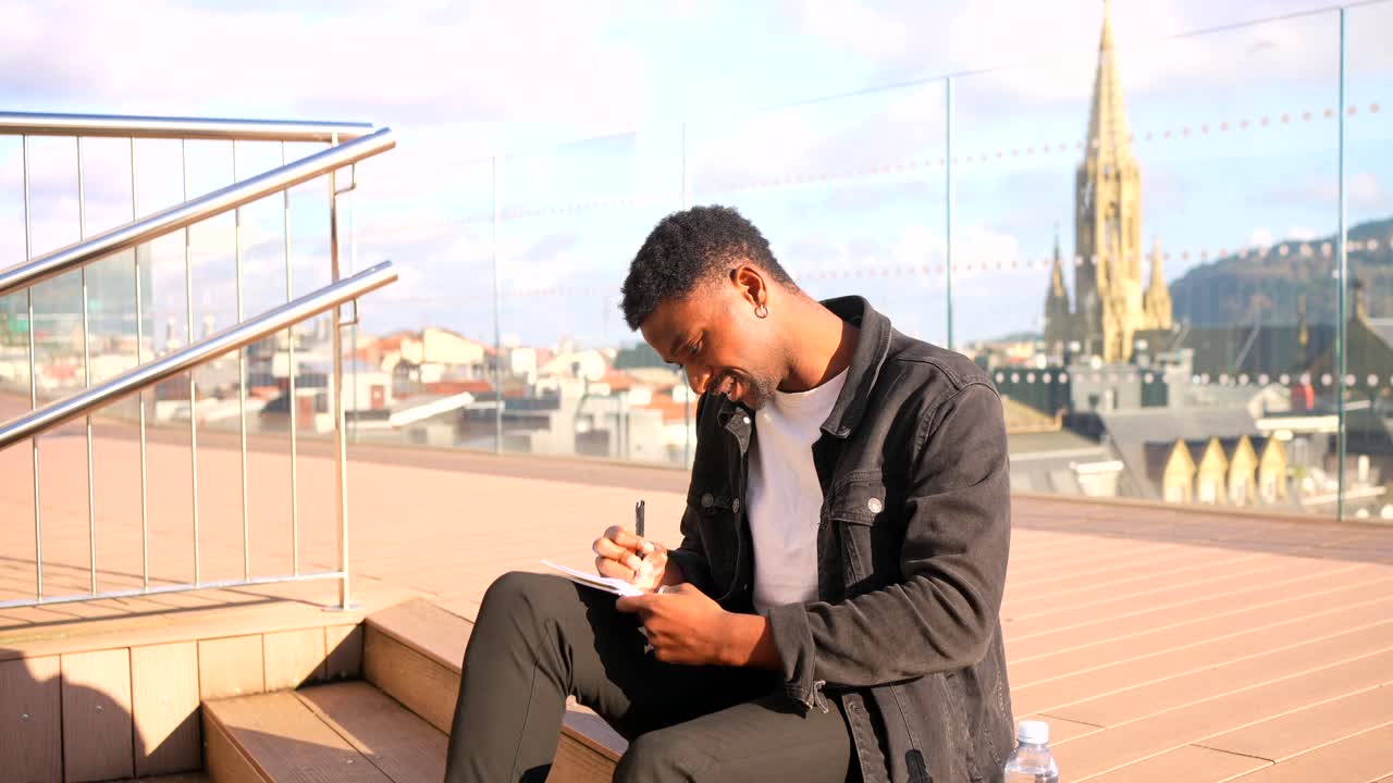 Man Writing on Rooftop with City View