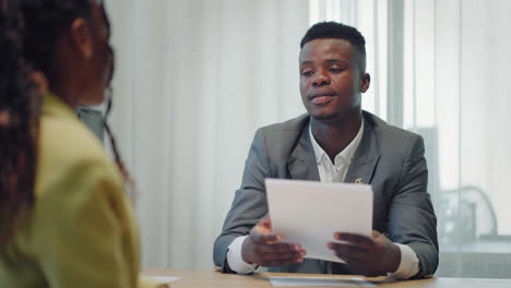 making a first impression. young black man meets potential employer in office for interview. welcome to the company. smiling black woman sitting at office desk and talking to during job interview