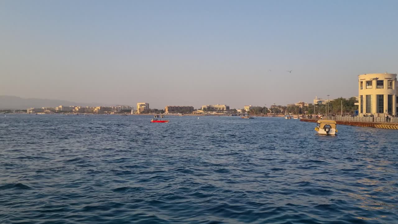 Sakin Kızıldeniz’in güneşli bir akşam ışığında panoramik manzarası, hafif sularda küçük tekneler ve uzak ufuk kıyılarında görülebilen Eilat (İsrail) ve Akabe’nin (Ürdün) silüeti