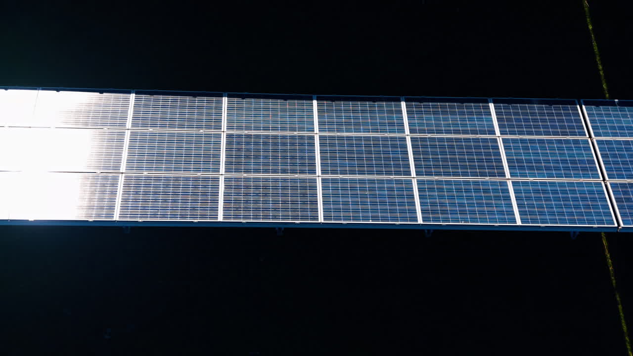 Vista aerea orizzontale di una fila di moduli di pannelli solari. Una singola fila di pannelli solari blu con riflesso del sole sul lato sinistro, vista aerea dall'alto