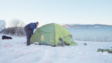 man assembling camping tent with ocean views at wintertime