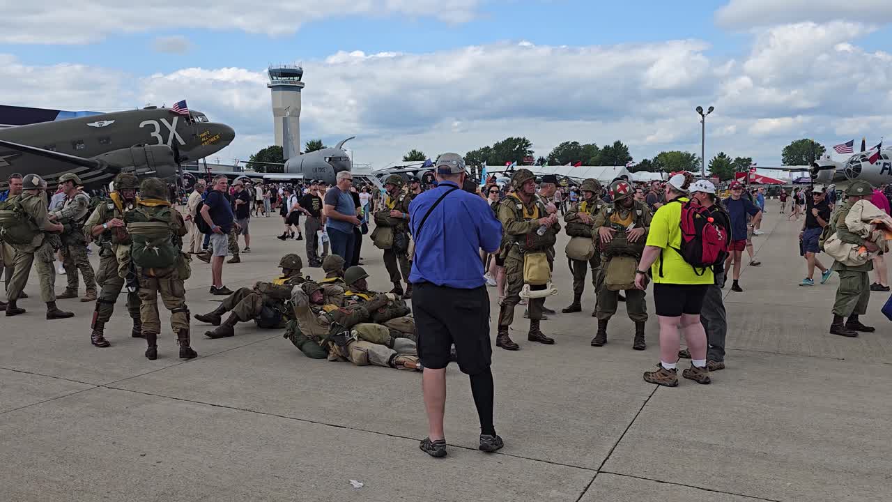 Historical reenactors dressed in vintage military uniforms gather near aircraft during the EAA AirVenture airshow in Oshkosh, Wisconsin.