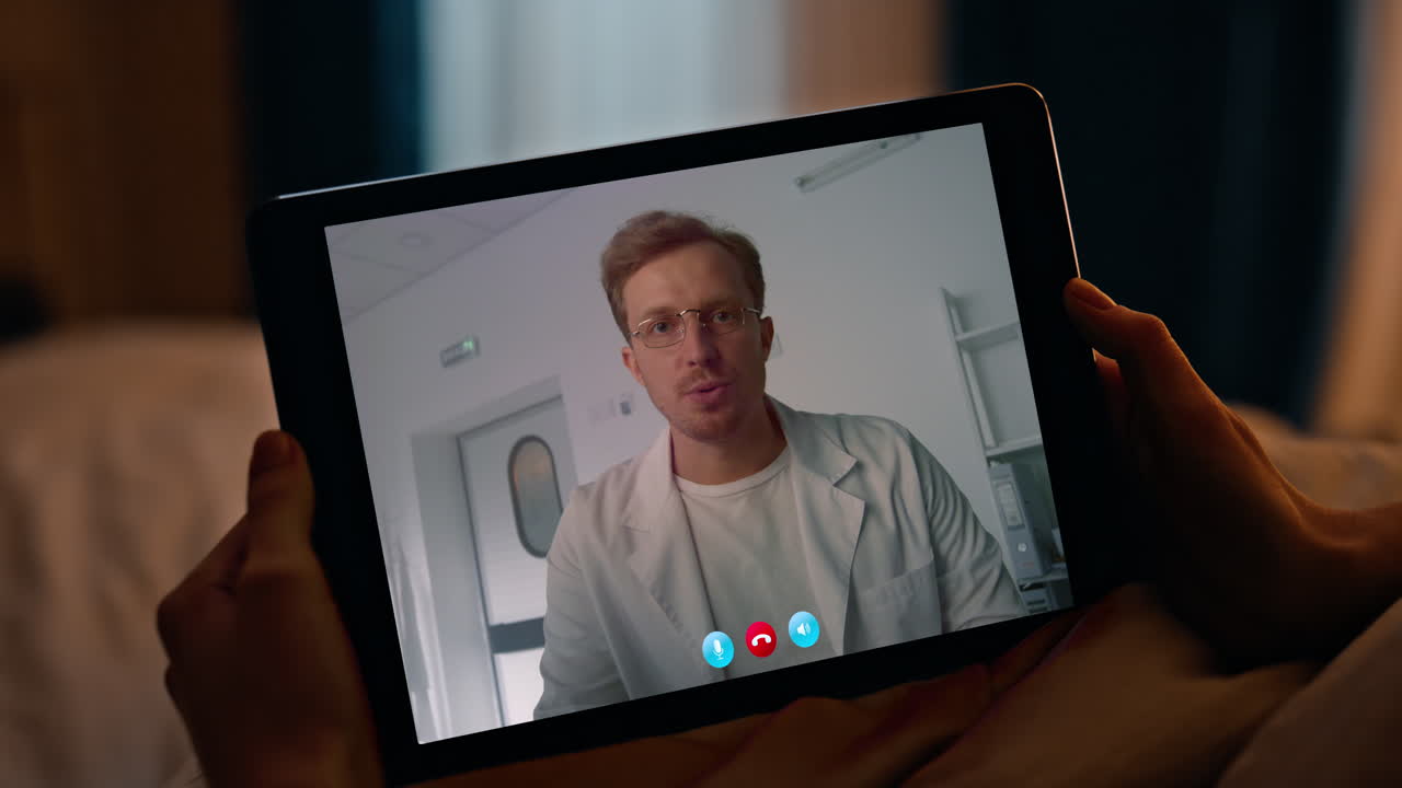 Donna malata che guarda lo schermo di un tablet mentre chiama un medico in webcam in una camera da letto serale, primo piano
