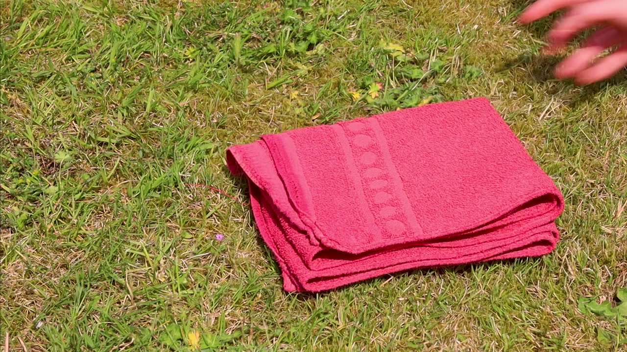 Video folding a red towel in the summer outside.