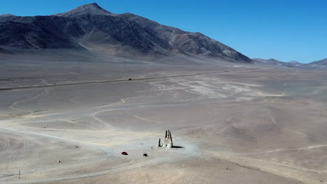 aerial orbits tourists at massive sculpted hand in chile desert sand