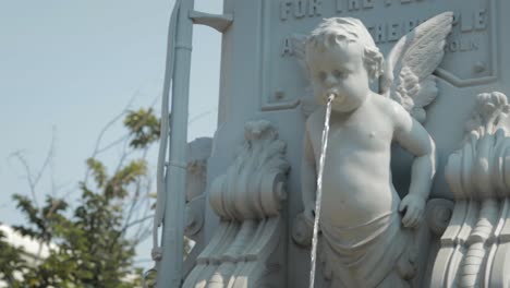 a cherub with wings spits water from a fountain