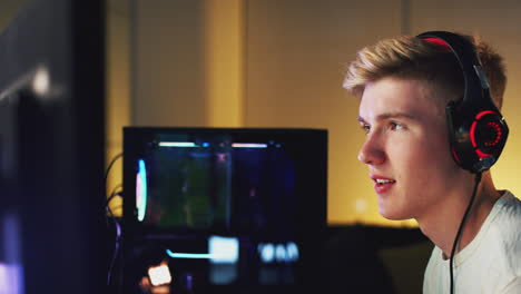 teenage boy wearing headset gaming at home using dual computer screens