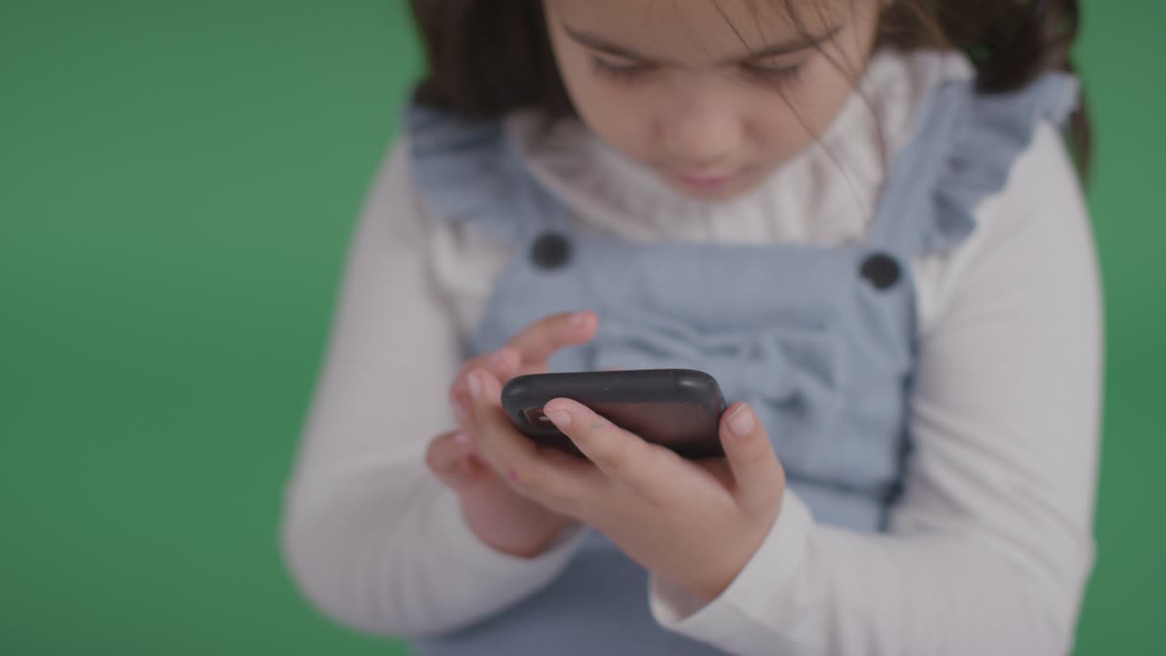 녹색 배경에서 휴대폰을 가지고 노는 asd 스펙트럼에 있는 어린 소녀의 스튜디오 초상화 1