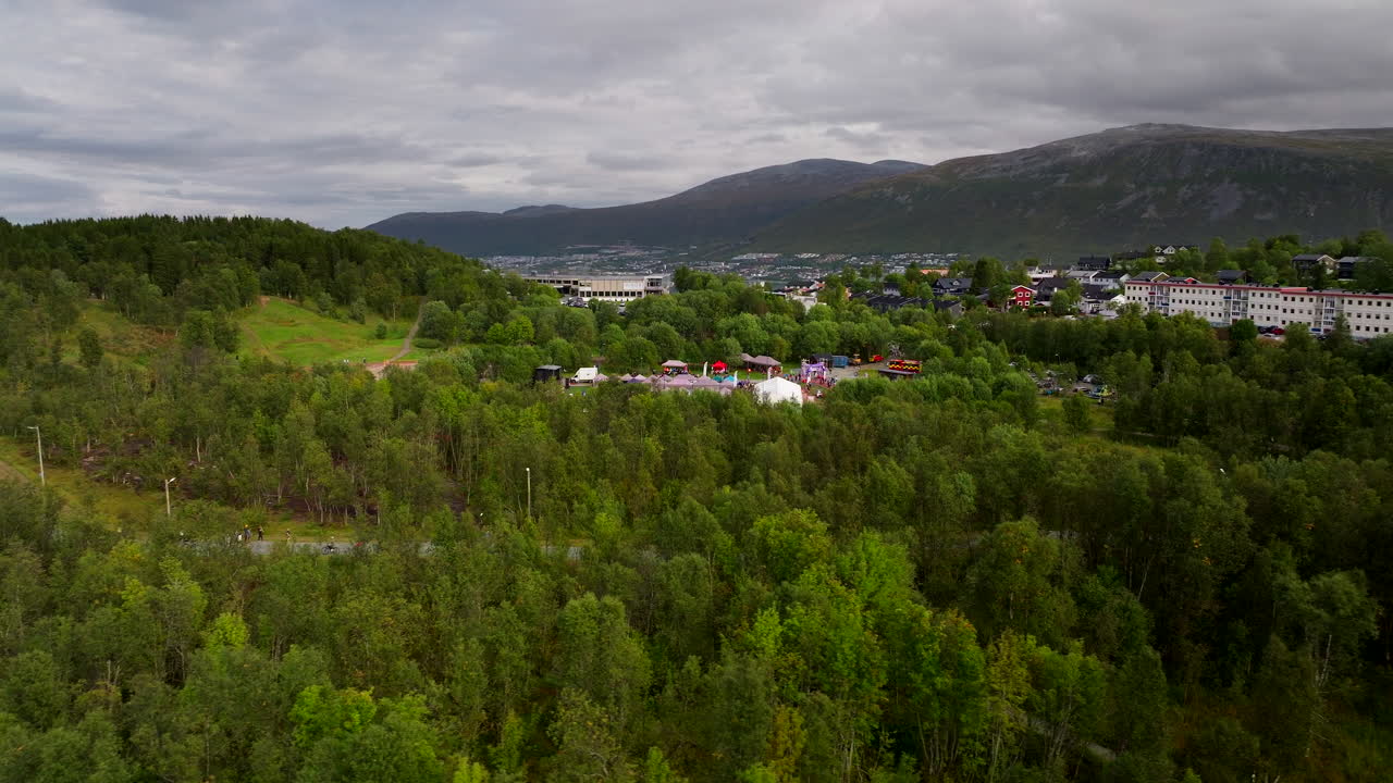 Drone orbits a charity relay gathering in Tromsø amid forested hills, Aerial