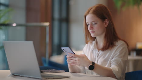 young woman is using smartphone for chating online in app during working day in office