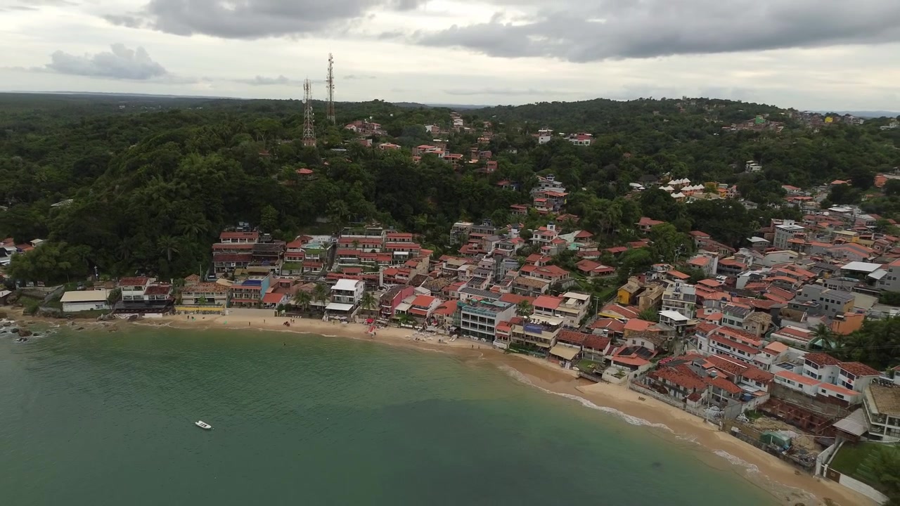 Riprese aeree con drone che si inclina verso l'alto e si allontana, rivelando la bellissima Prima Spiaggia e il villaggio costiero a Morro de Sao Paulo, Bahia, Brasile.