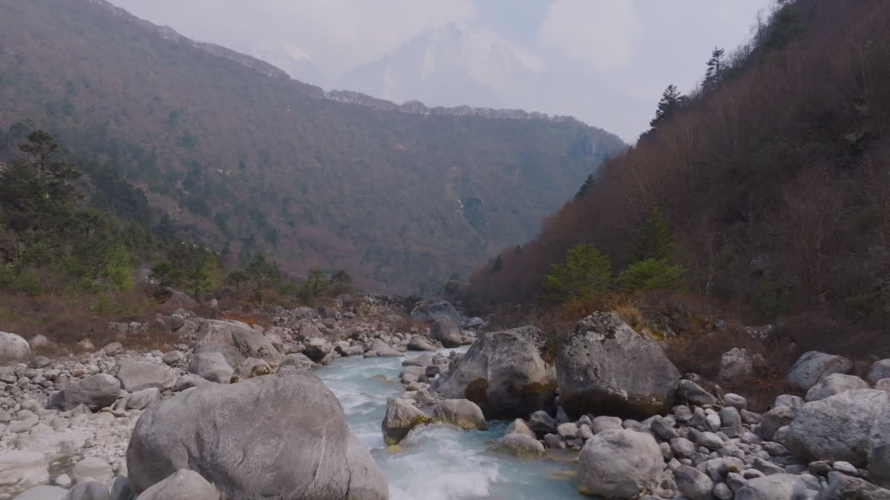 Drone shot of Dudhkoshi River on route to Everest, flowing through hilly terrain and rocky banks under clear sky. Adventure travel in Nepal with serenity of Mountain range and natural resources