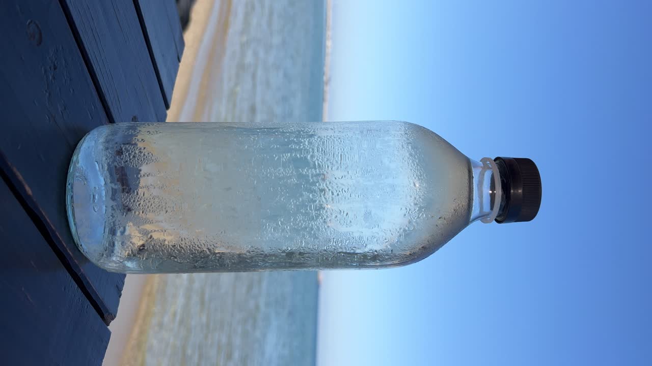 primer plano de la botella de agua fría de condensación contra el fondo del mar griego