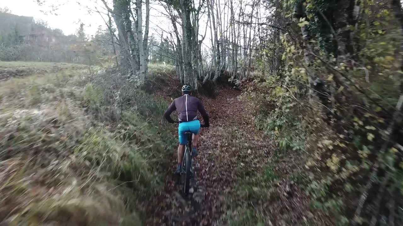Low flight drone following mountain biker on a trail in the woods in Italy