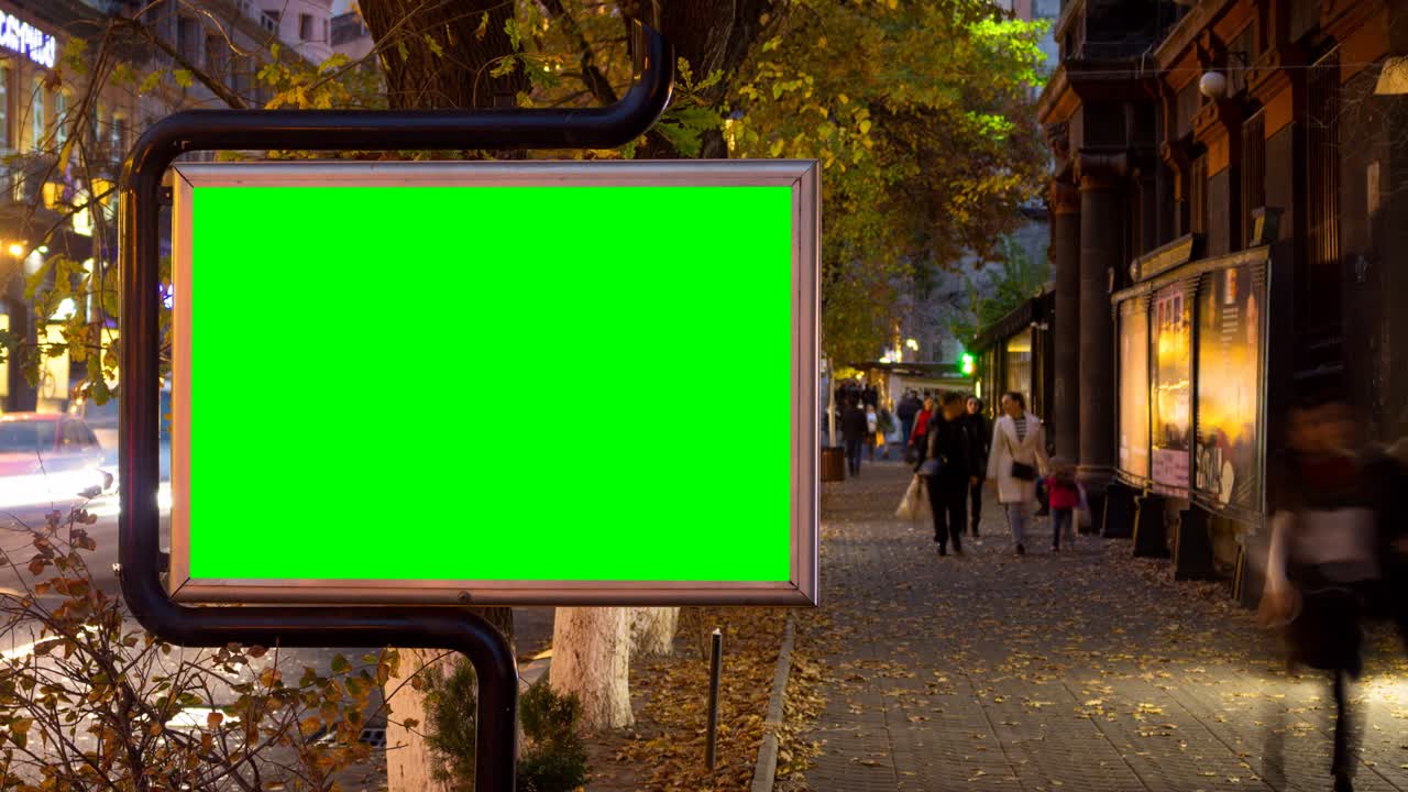 Video 4K in time lapse. Grande cartellone pubblicitario con schermo verde sullo sfondo di persone sfocate che camminano in una città autunnale.