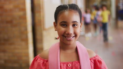 Portrait-of-happy-mixed-race-schoolgirl-standing-in-corridor-looking-at-camera