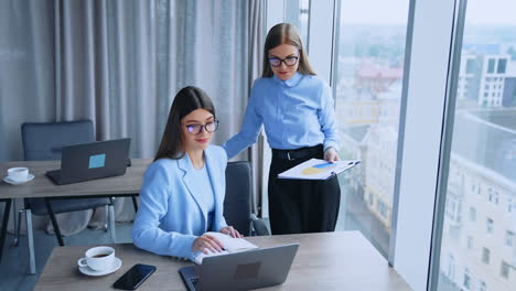 young women colleagues at work talking looking at laptop. relaxed friendly communication among the coworkers.
