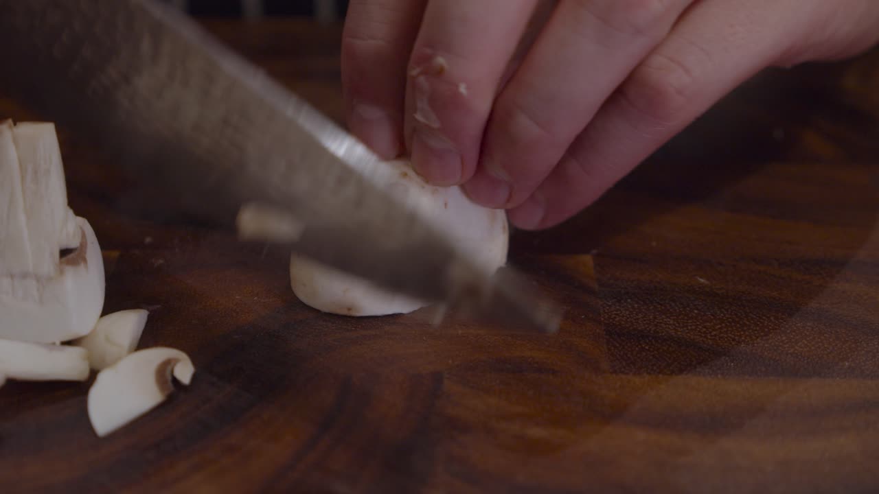 Chef cuts white mushrooms on wooden cut board in the kitchen